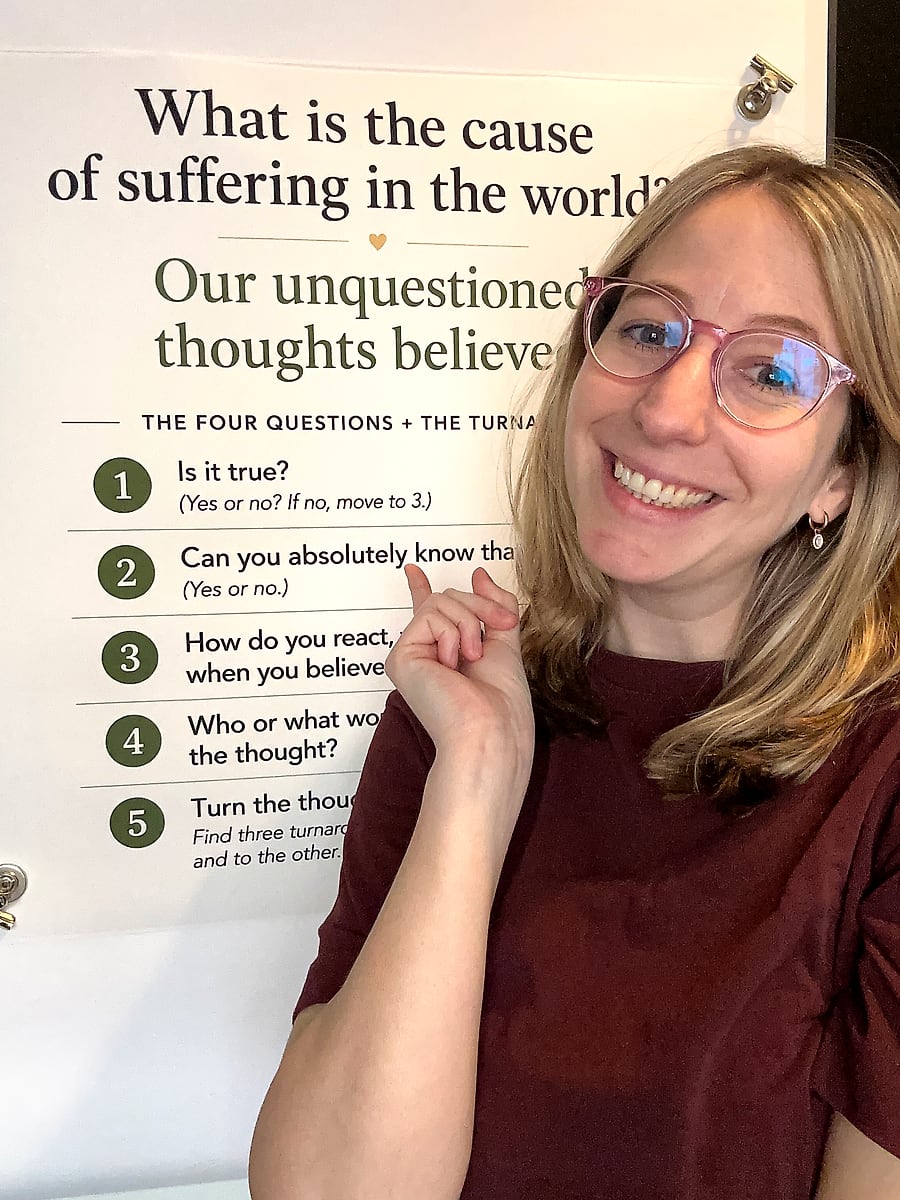 Tamara with a big smile, pointing at her poster of Byron Katie's four questions, starting with: Is it true?