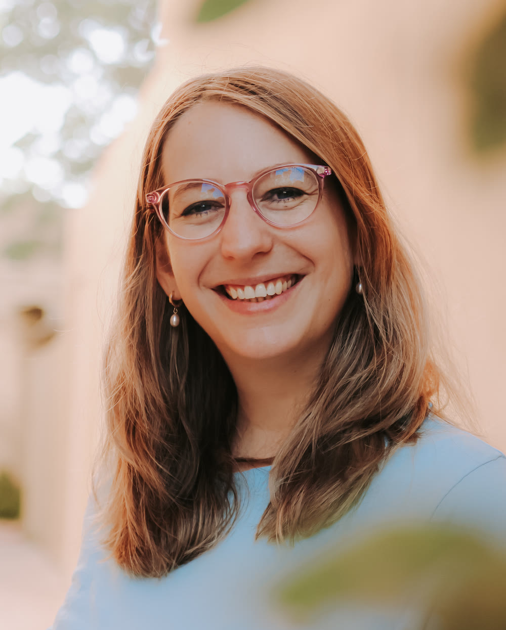Tamara smiling at the camera in a light blue t-shirt, leaves in front of her